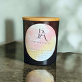 A scented candle with a label reading 'JA Tabacco Velvet', placed on a reflective surface.