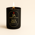 Lit New Dawn Candle by Josie’s Aroma in a black holder with gold text, luxury scented home fragrance product