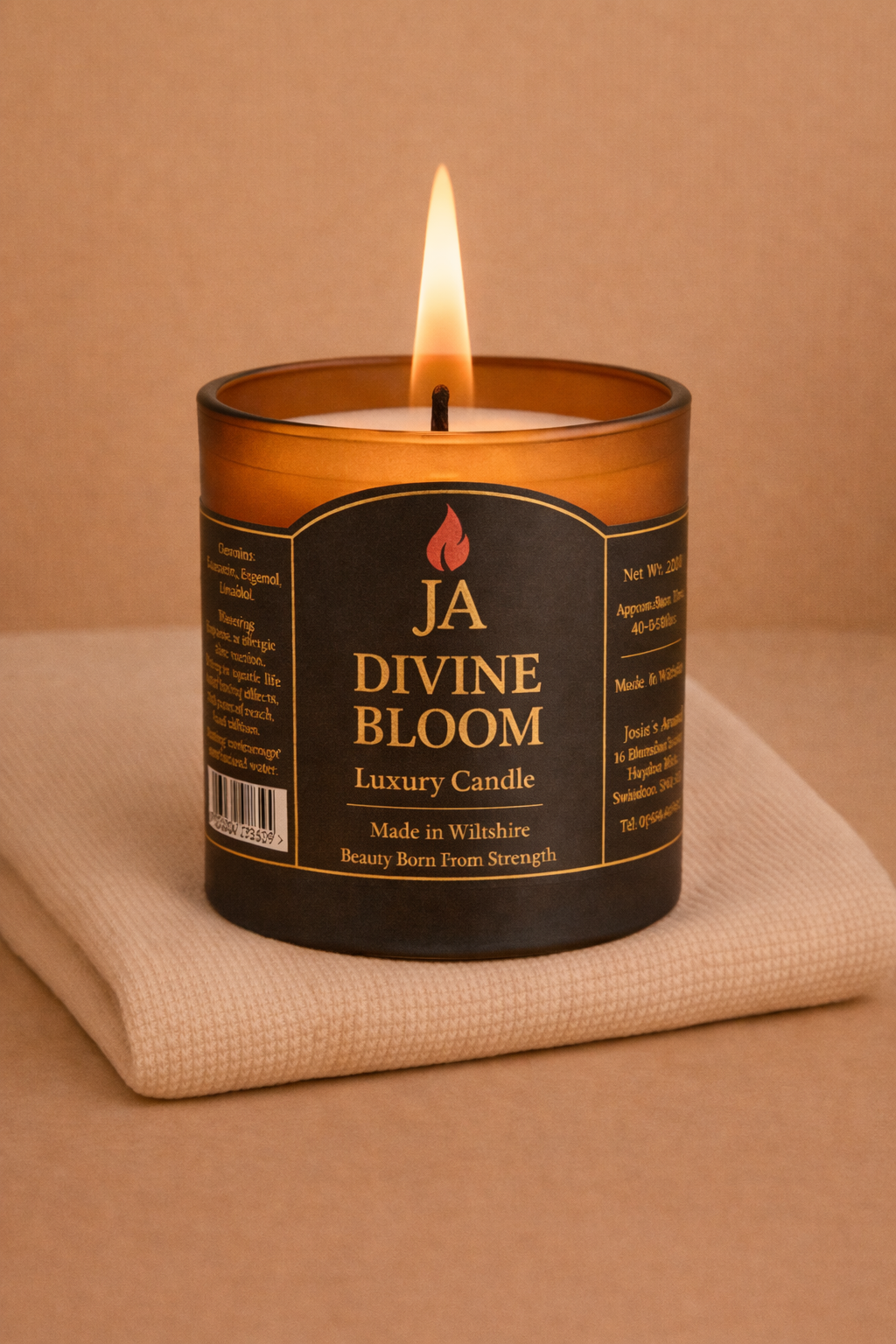 Lit Divine Bloom luxury candle in amber glass jar on beige fabric, creating a cozy and elegant home ambiance