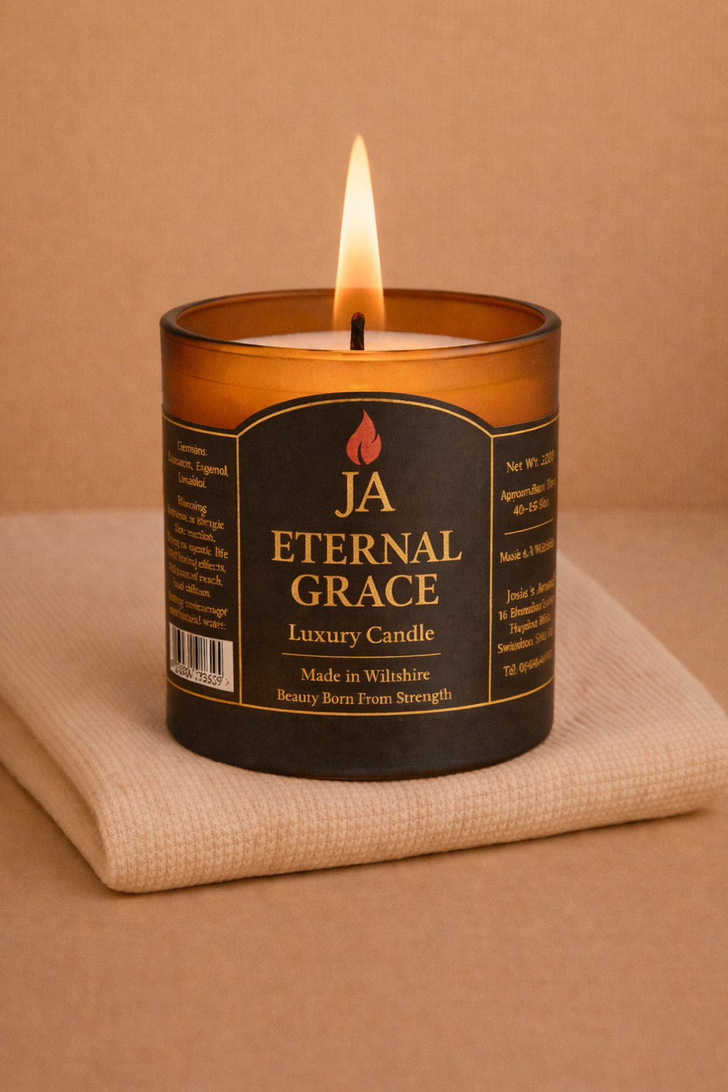 Lit Eternal Grace luxury candle in amber glass on a soft beige cloth, creating a calming cozy atmosphere.