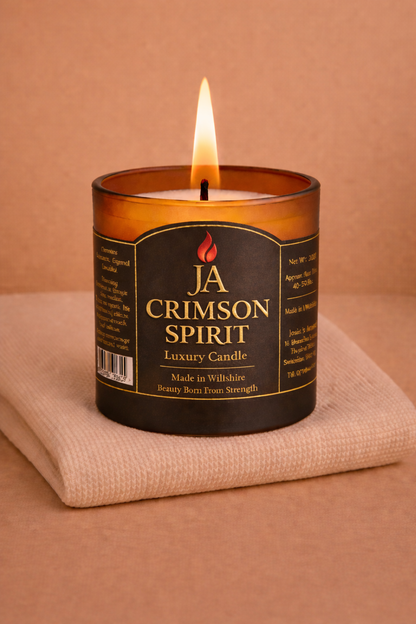 Lit JA Crimson Spirit luxury black pomegranate candle on beige cloth with warm brown background